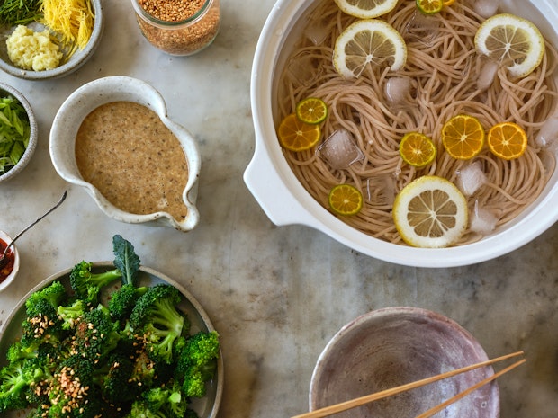 Noodles που επιπλέουν σε παγωμένο νερό που περιβάλλεται από γαρνιτούρες και σάλτσα σουσάμι σε ένα τραπέζι