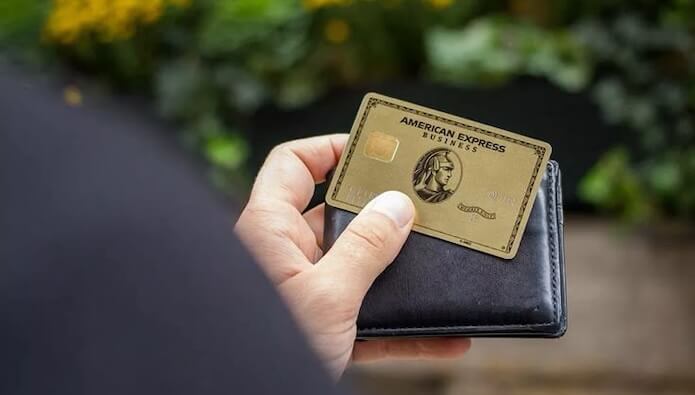 Η χρυσή κάρτα American Express® συγκρατείται μπροστά σε ένα φωτεινό μπλε τοίχο